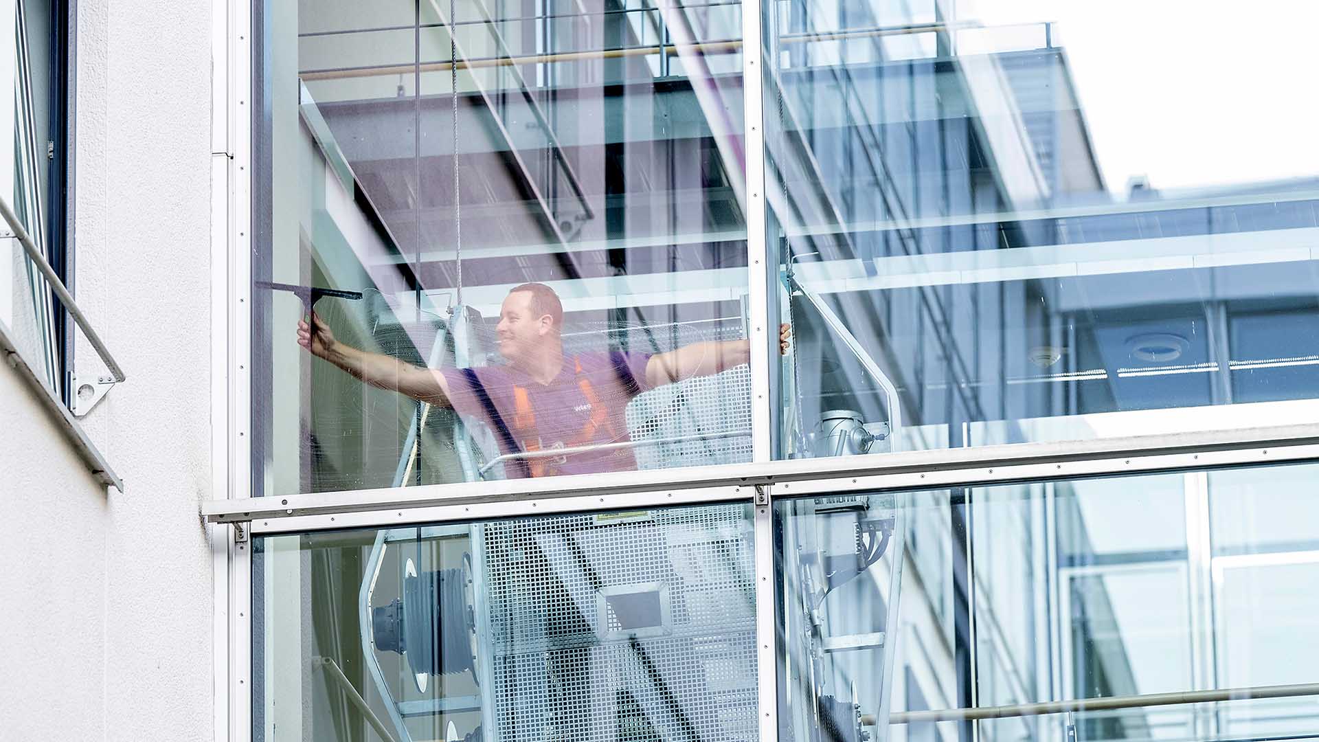 Reinigungskraft im Korb reinigt Glasfläche
