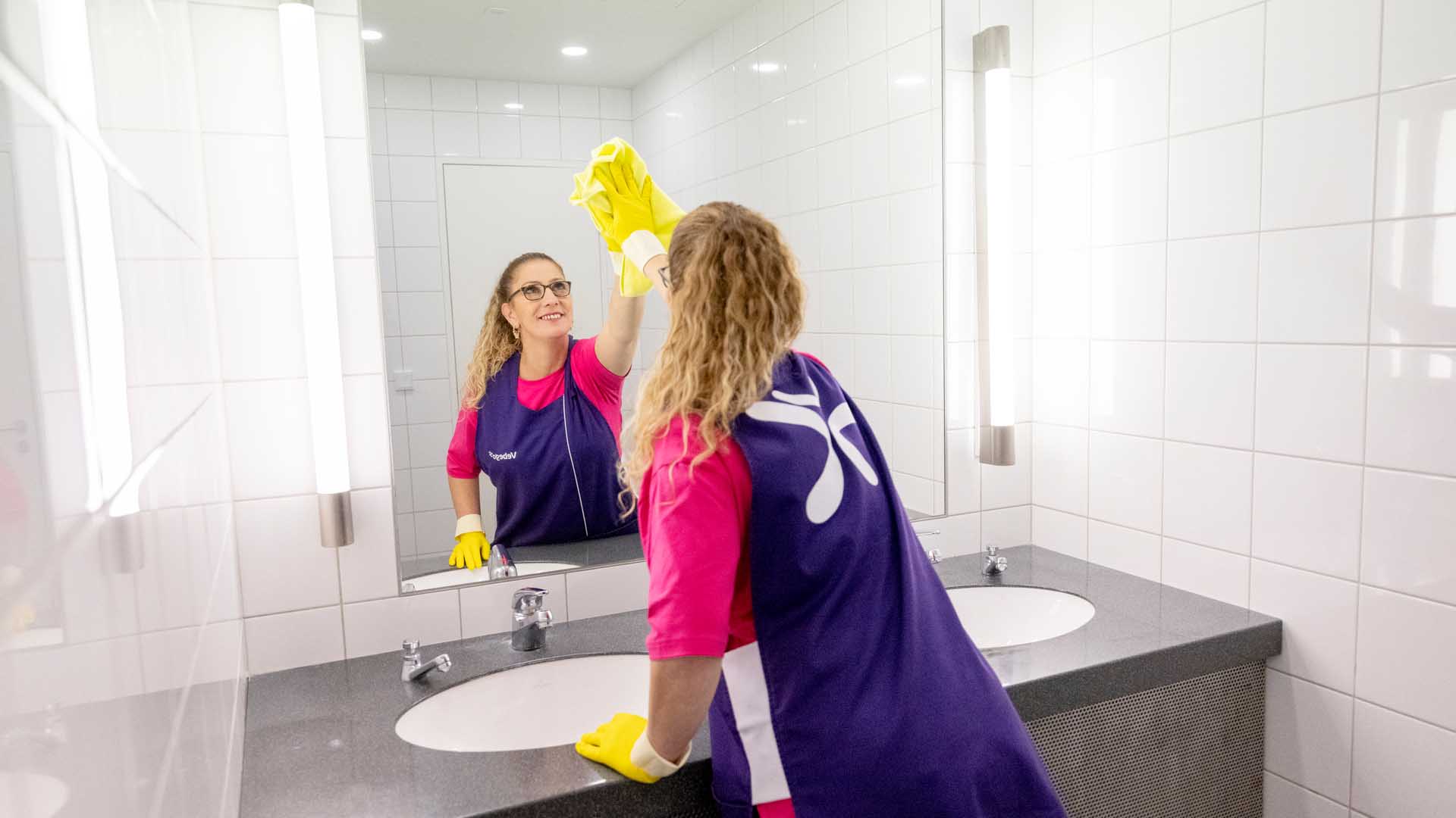Reinigungskraft reinigt Spiegel im Sanitärbereich